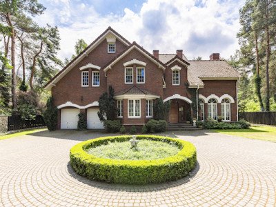 Front view of a driveway with a round garden and big, english style house in the background. Real photo